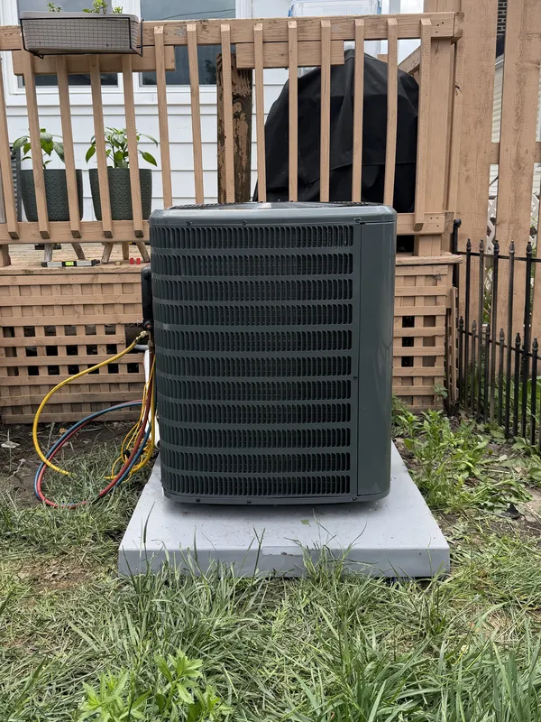 New outdoor AC unit on a pad in front of a wooden deck, with refrigerant gauge hoses connected, in Cleveland, OH