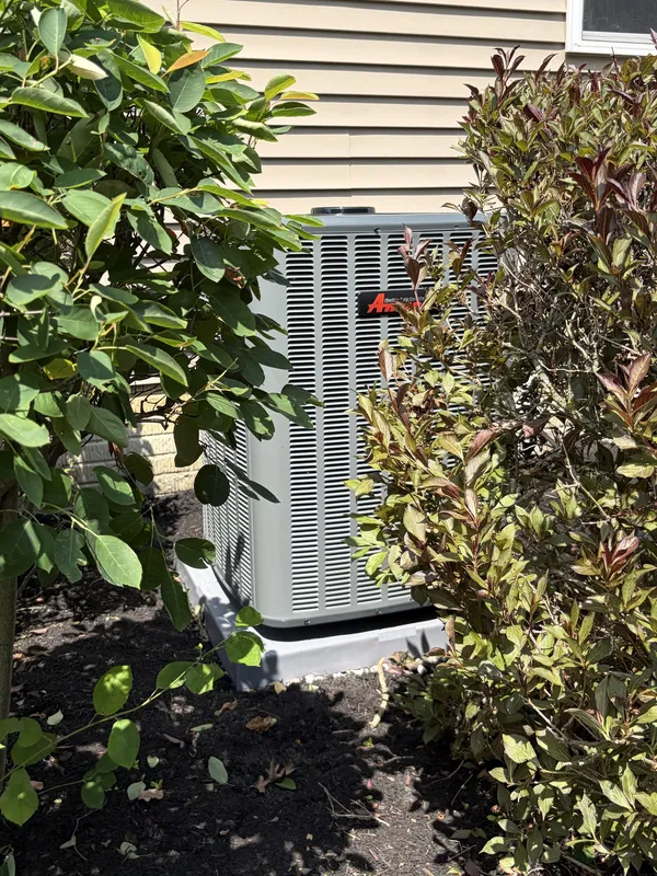 New outdoor AC unit on a pad between two shrubs beside a house in North Ridgeville, OH