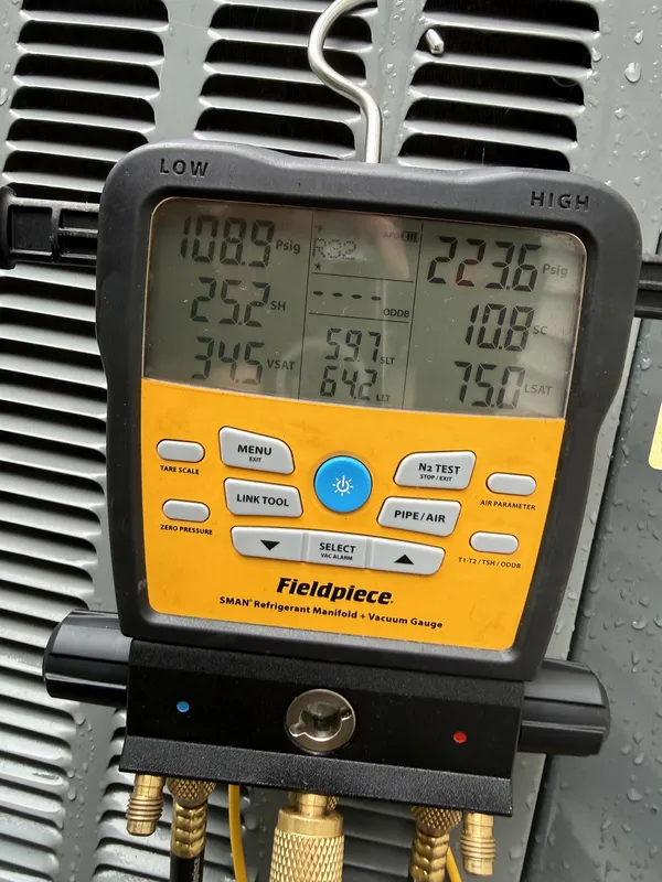 Refrigerant gauge hung on a rain-wet outdoor AC unit during an AC tune-up in Avon Lake, OH