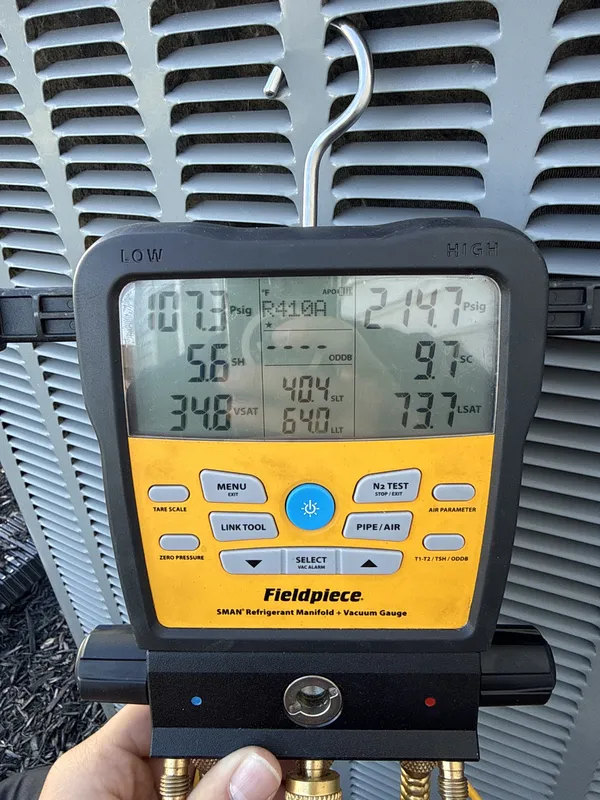 Technician holding a refrigerant gauge in front of the outdoor AC unit during an AC tune-up in North Ridgeville, OH