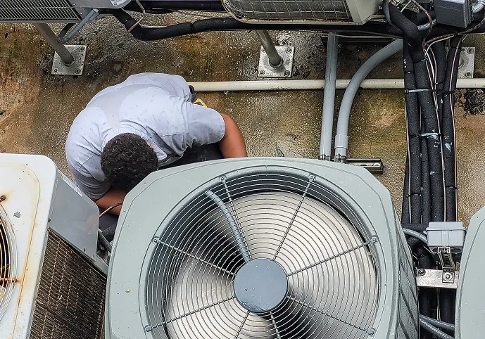 Technician kneeling between outdoor AC condenser units, seen from above