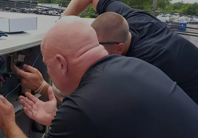 Two Anderson technicians checking the wiring inside a rooftop AC unit