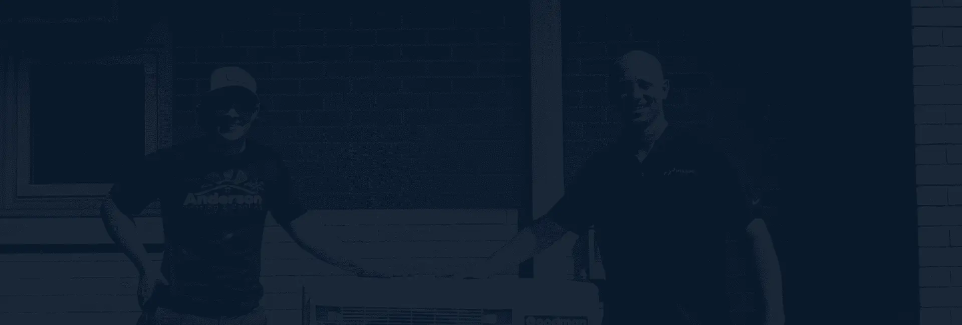 Two men standing outside a brick house, one in an Anderson Heating and Cooling shirt