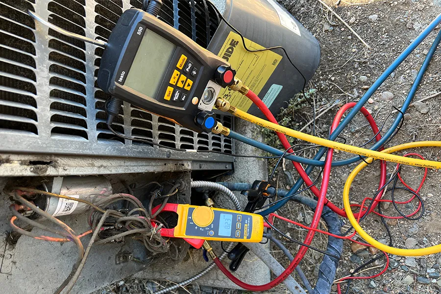 Digital refrigerant gauge and a clamp meter hooked up to an outdoor AC unit