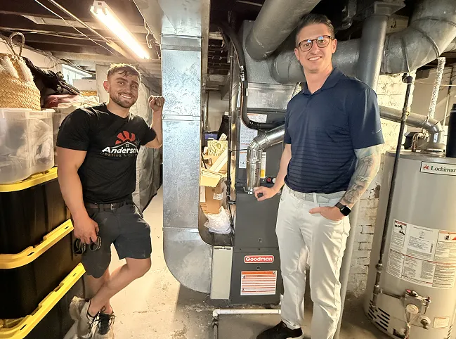 Two Anderson Heating and Cooling team members beside a gas furnace in a basement