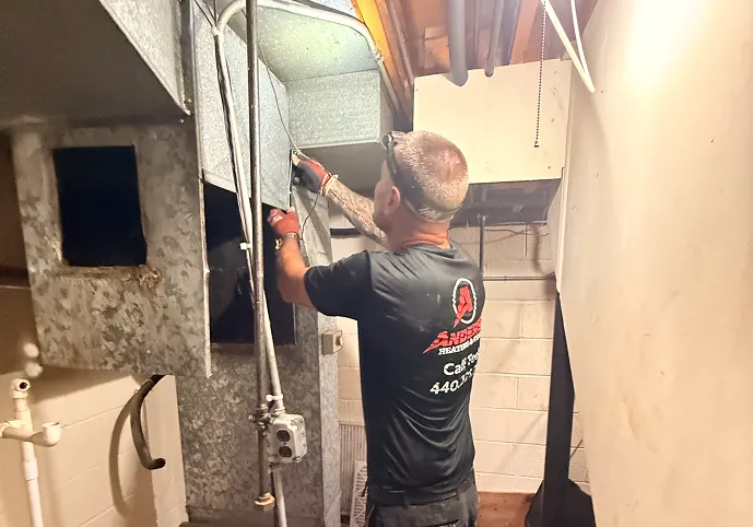 Anderson technician working on the ductwork above a basement furnace