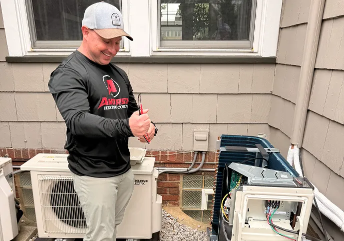 Anderson technician with wire strippers beside two outdoor units, one with its cover off