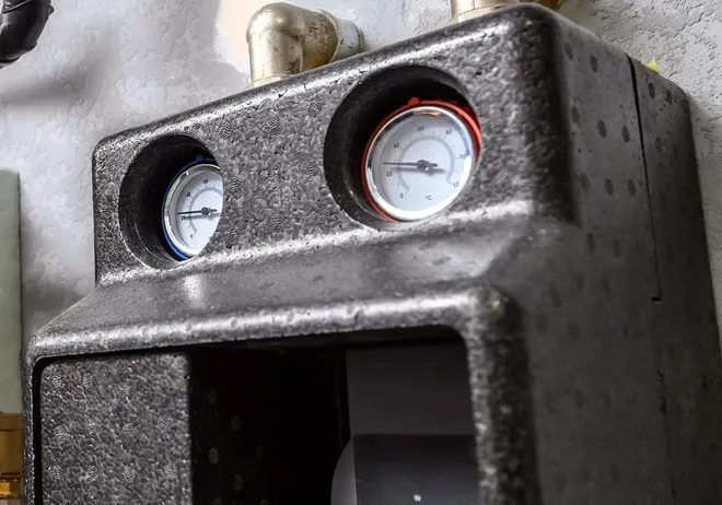 Insulated pump housing with blue and red temperature gauges on a hot water heating system