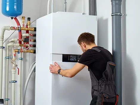 Technician checking a white wall-mounted boiler, with its water pipes and expansion tank beside it