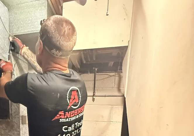 Anderson technician working on the sheet-metal ductwork of a basement furnace