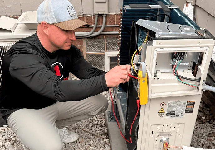 Anderson technician testing the wiring of a heat pump outdoor unit with a clamp meter