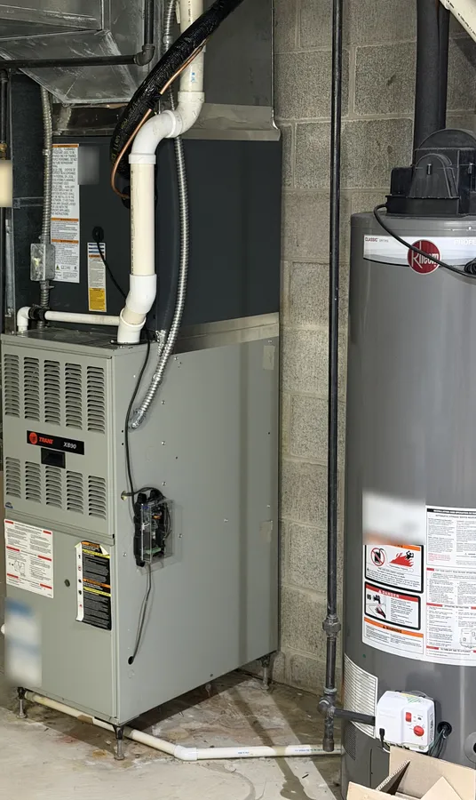 Gas furnace with white plastic vent pipes beside a gas water heater in a basement