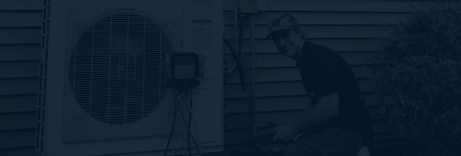 Technician kneeling beside an outdoor unit with a refrigerant gauge hooked up