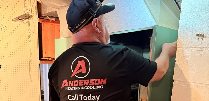 Anderson Heating and Cooling technician opening the cabinet of a basement furnace